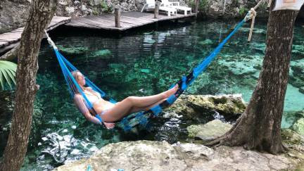 A visitor swinging on a hammock across a cenote