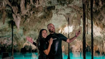 A couple standing in a cenote cave with stalactites and stalagmites